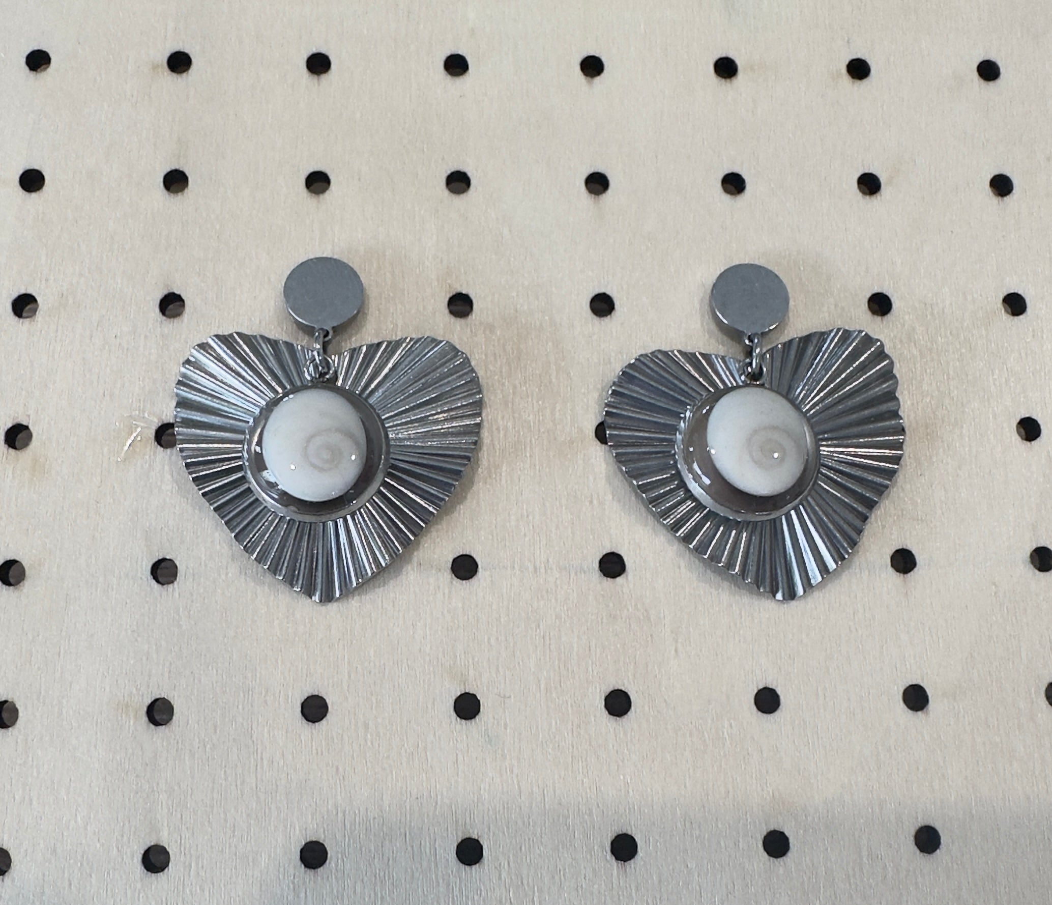Vue rapprochée des boucles d'oreilles Astra argentées, pendentif cœur à rayons et cabochon Oeil de Sainte-Lucie