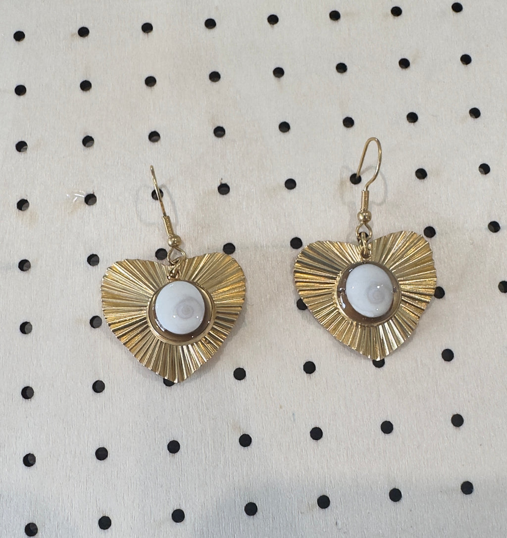 Vue rapprochée des boucles d'oreilles Astra dorées, pendentif cœur à rayons et cabochon Oeil de Sainte-Lucie