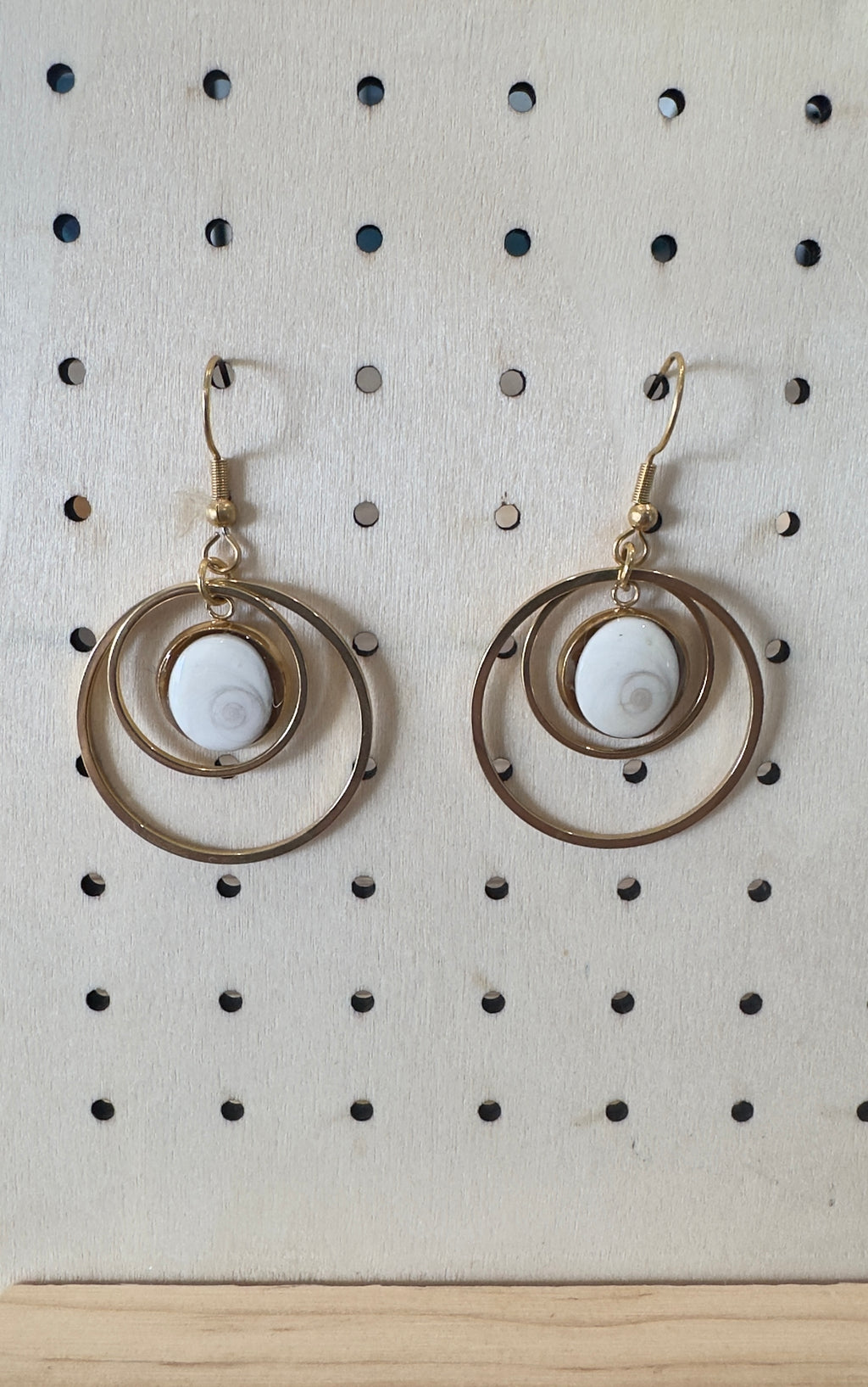 Gros plan sur les cercles concentriques dorés et le cabochon Œil de Sainte-Lucie des boucles d'oreilles Halo
