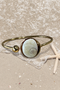 Bracelet jonc doré avec médaillon rond serti d'un Œil de Sainte-Lucie, style minimaliste marin.
