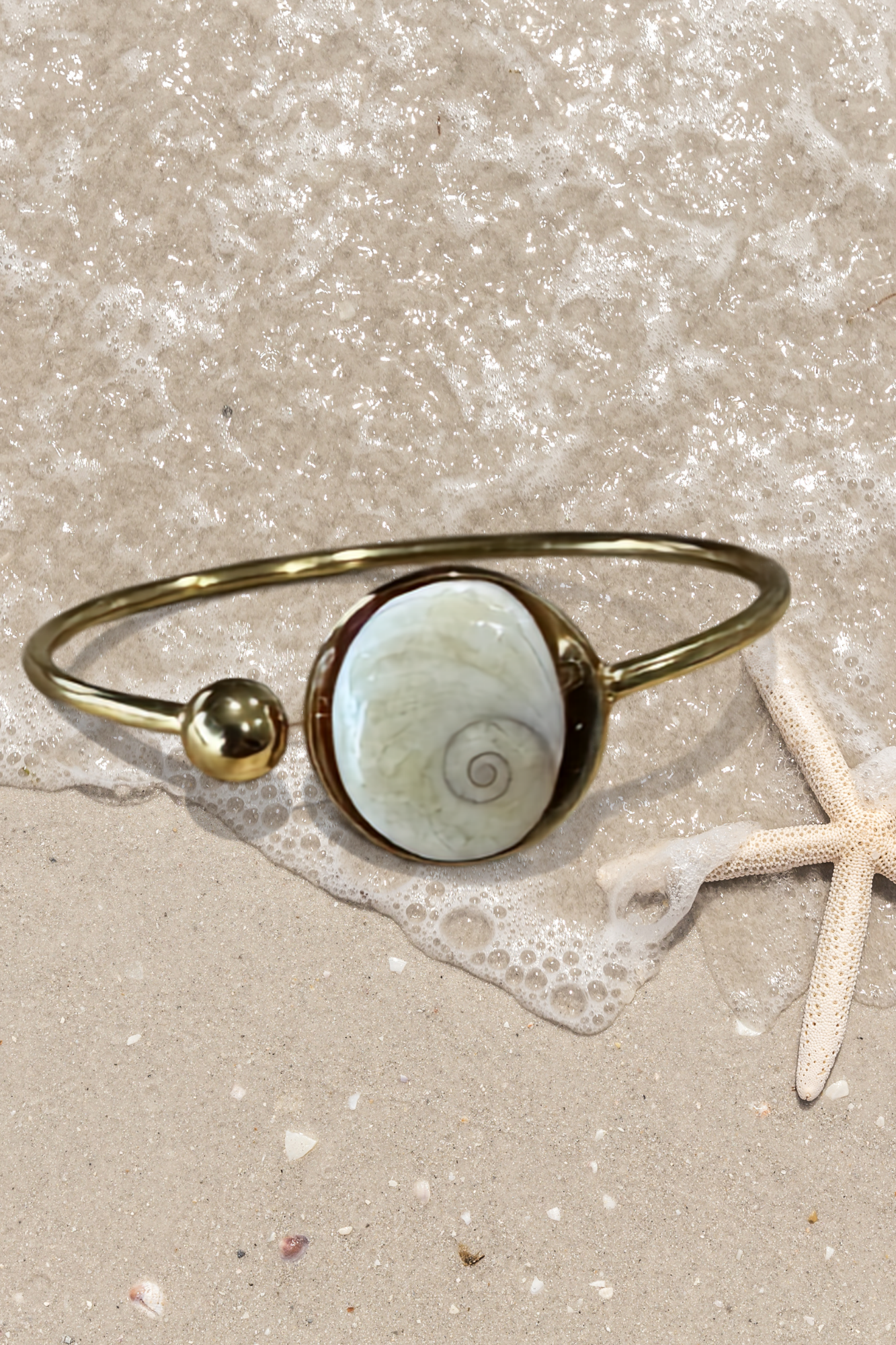 Bracelet jonc doré avec médaillon rond serti d'un Œil de Sainte-Lucie, style minimaliste marin.