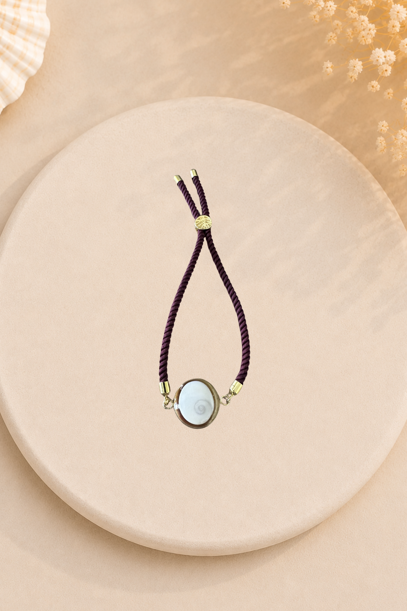 Bracelet femme Œil de Sainte‑Lucie sur cordon aubergine et médaillon doré. Bijou artisanal, chic et porte‑bonheur méditerranéen, élégant au quotidien.
