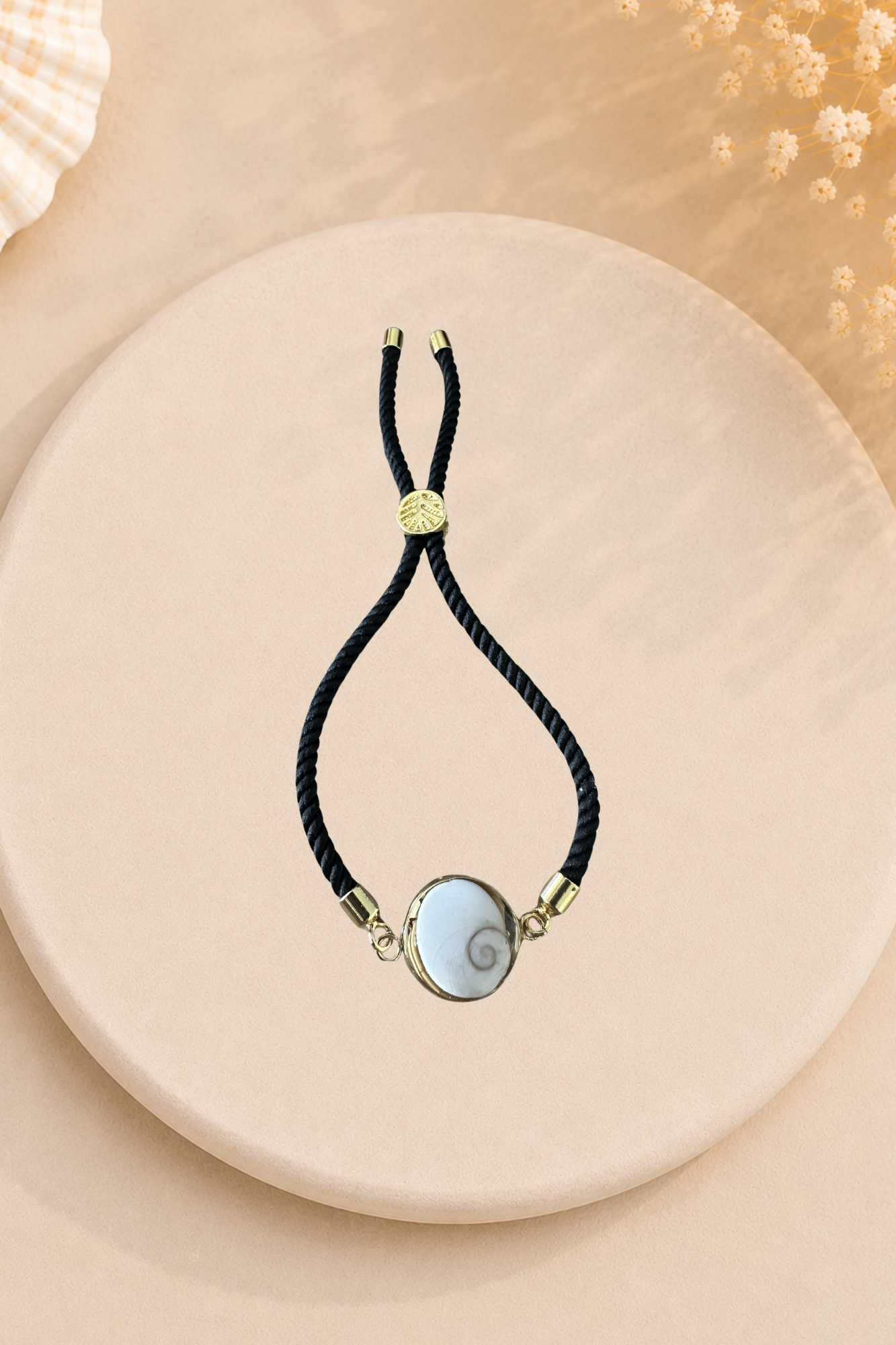 Bracelet femme Œil de Sainte‑Lucie sur cordon noir et médaillon doré. Bijou artisanal, chic et porte‑bonheur méditerranéen, élégant au quotidien.