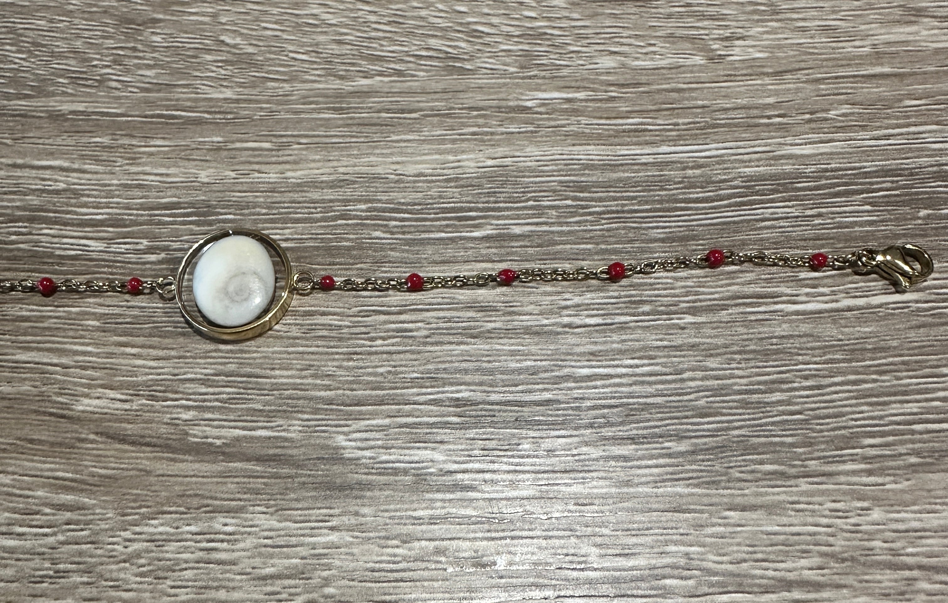 Gros plan sur le cabochon en Œil de Sainte-Lucie et les perles rouge du bracelet Thetis