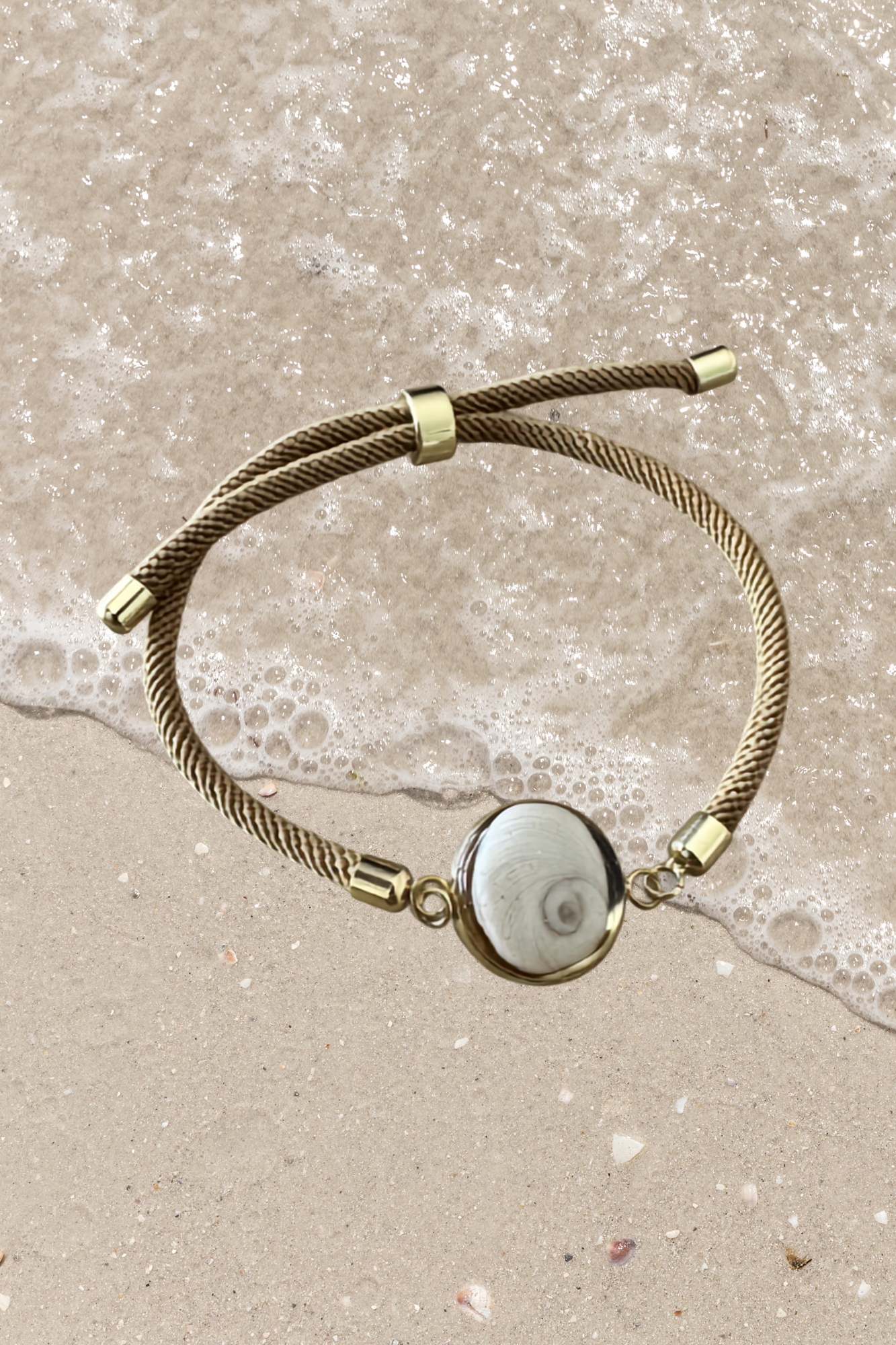 Bracelet femme, cordon marron beige fin, médaillon rond doré serti d’un Œil de Sainte‑Lucie blanc, style chic et minimaliste.